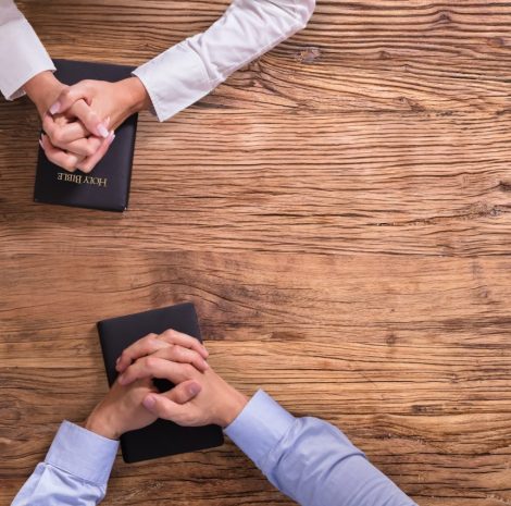 High,Angle,View,Of,People's,Praying,Hands,On,Holy,Bible